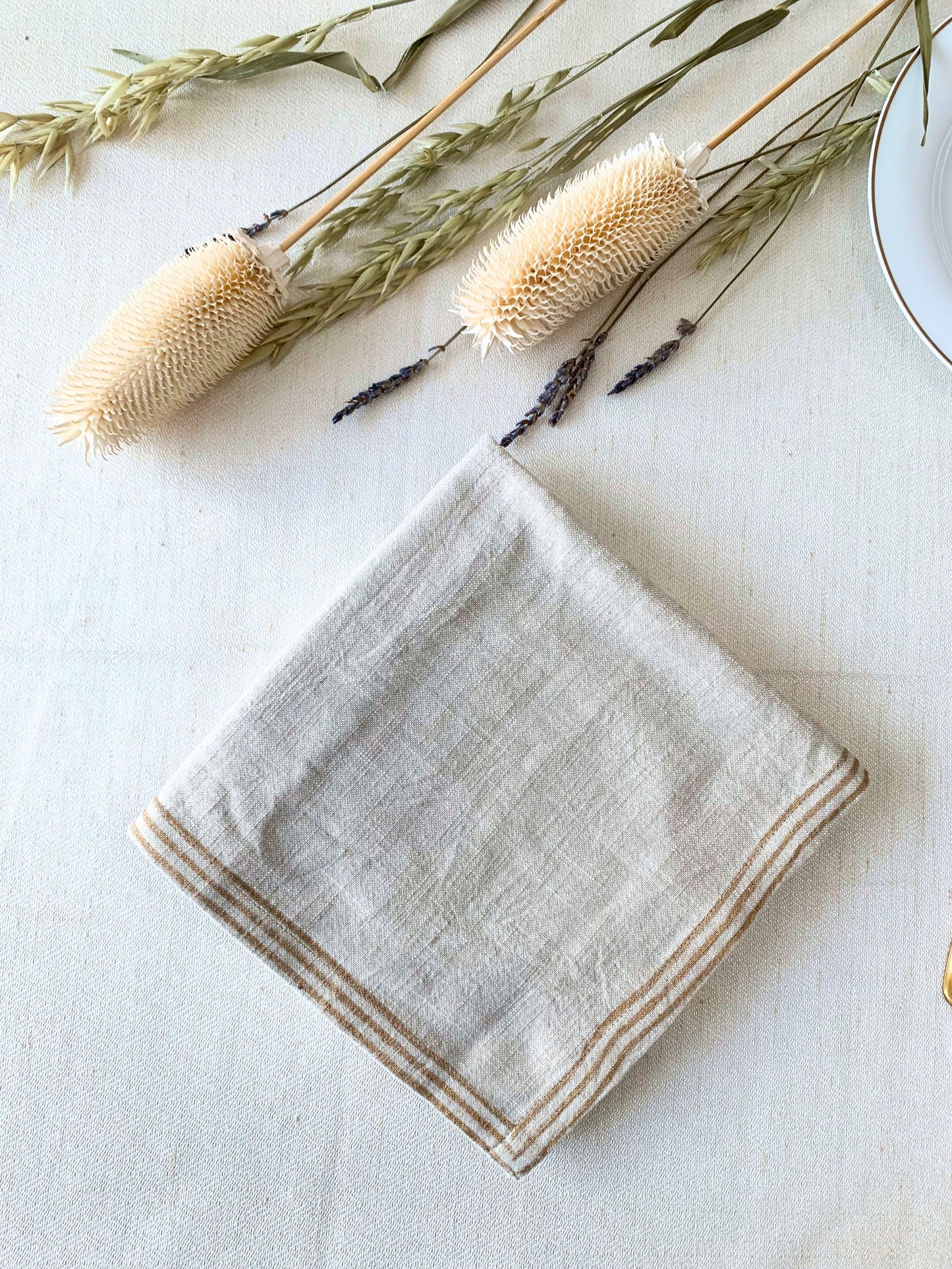 Upgrade your dining experience with this set of 6 napkins, crafted from GOTS certified organic cotton, showcasing dull gold block printed lines on a natural-beige fabric for a stylish and sustainable choice.