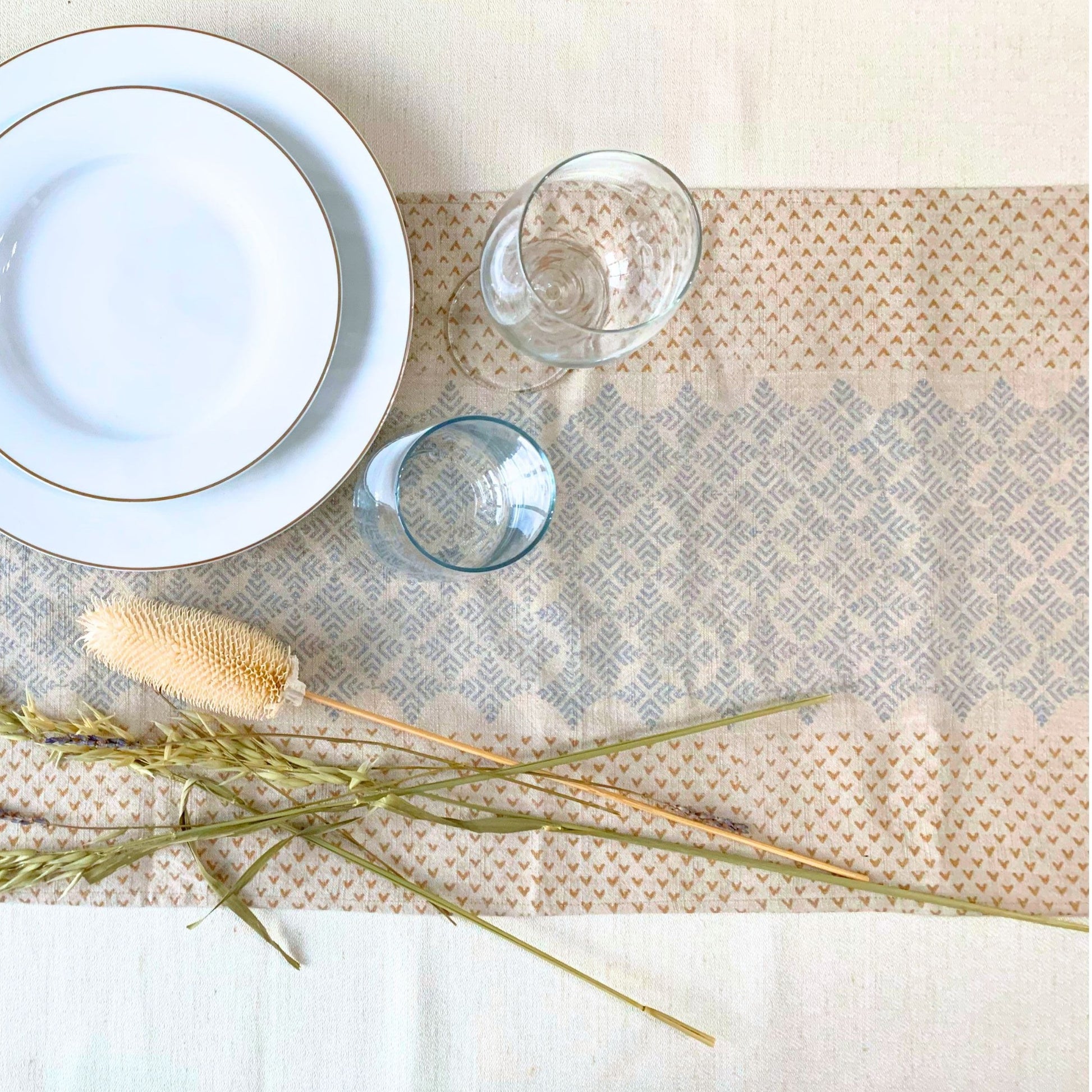 Crafted with sustainability in mind, this GOTS certified organic cotton table runner features an elegant geometric pattern, block-printed with dull gold and silver accents on a natural-beige fabric.