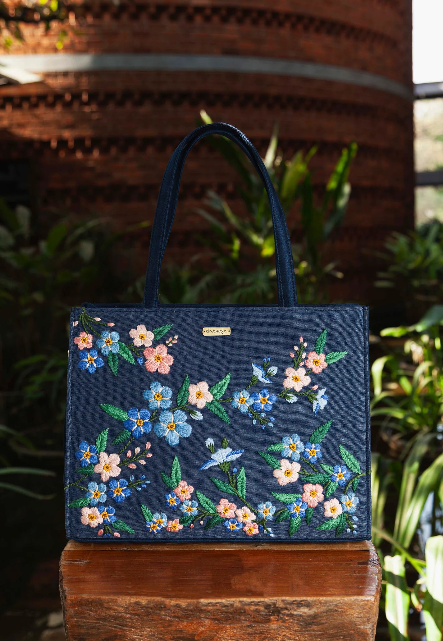 our Forget Me Not Tote Bag, a handcrafted masterpiece featuring delicate hand-embroidered flower bunches on navy-colored sustainable fabric.