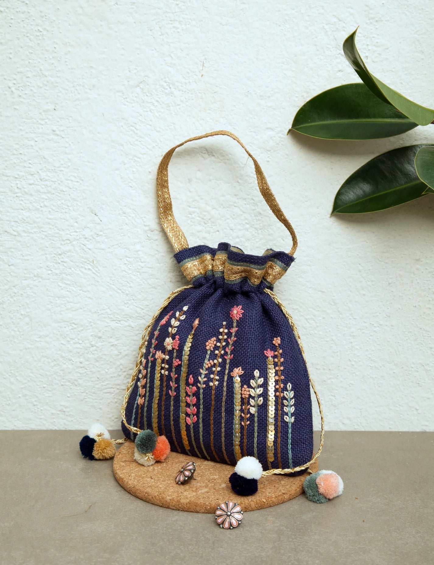 Hand-embroidered Floral Potli bag with intricate details and metal sequin embellishments, portraying a flower field. Perfect for ethnic and festive occasions, featuring elegant pom poms, a lace handle, and a drawstring closure for a luxurious touch.