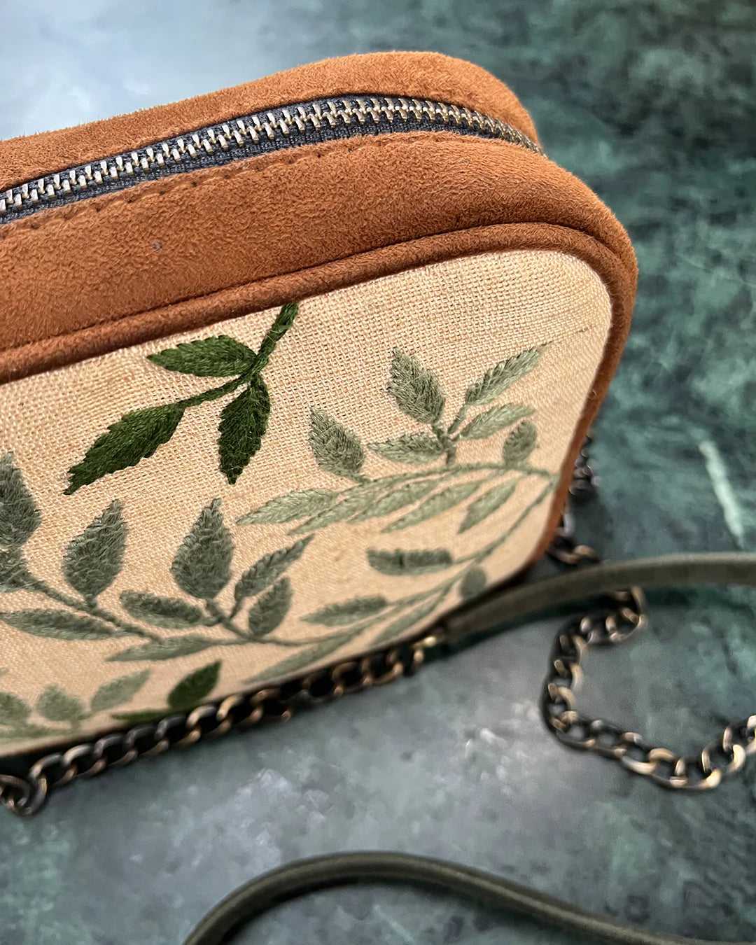 This compact bag features detailed hand embroidery on a premium vegan suede body, offering a touch of artistry and sophistication.