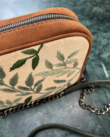 This compact bag features detailed hand embroidery on a premium vegan suede body, offering a touch of artistry and sophistication.