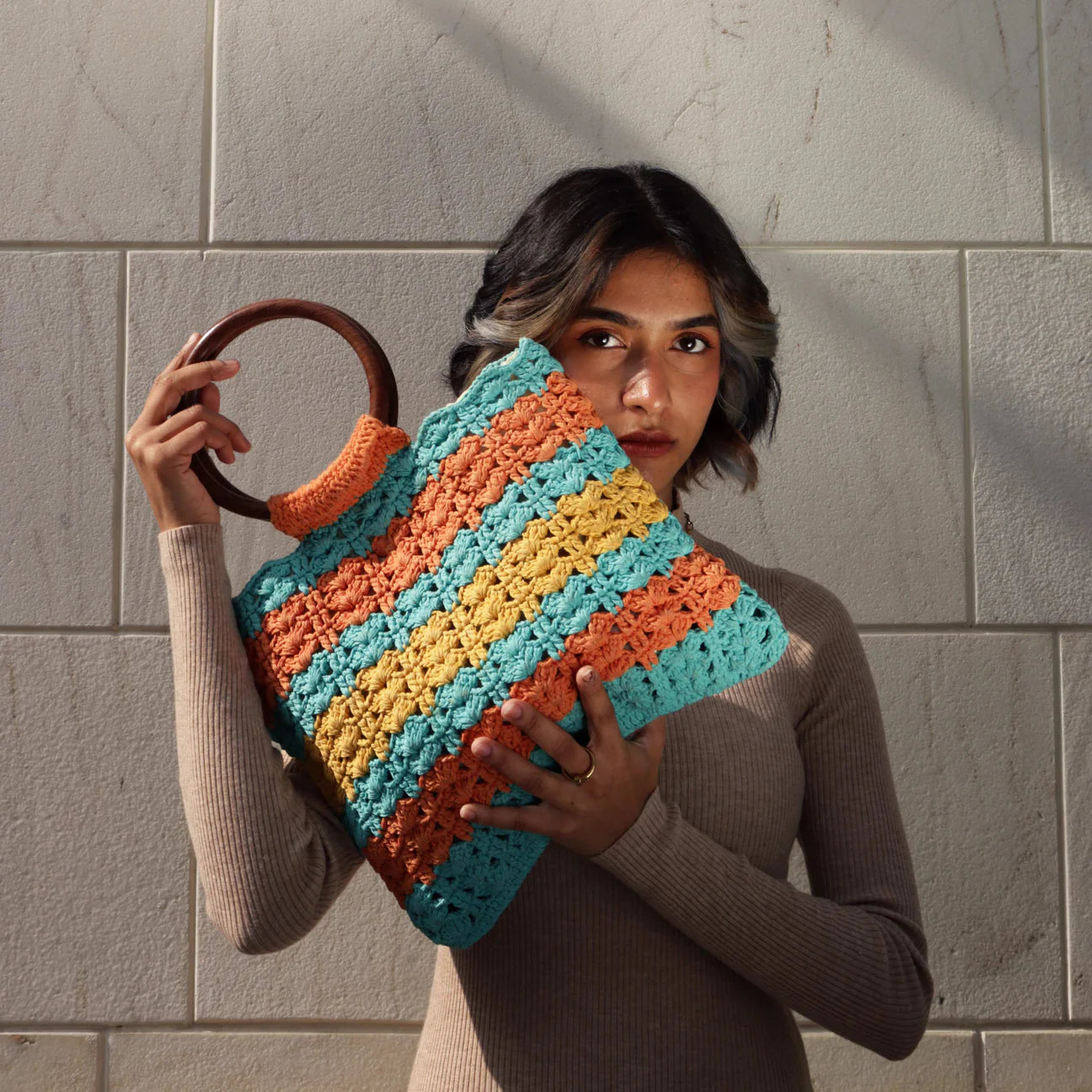 Enhance your style with our hand-crocheted rectangular handbag, featuring circular wooden handles, in vibrant hues of orange, blue, and yellow for a bold and chic look