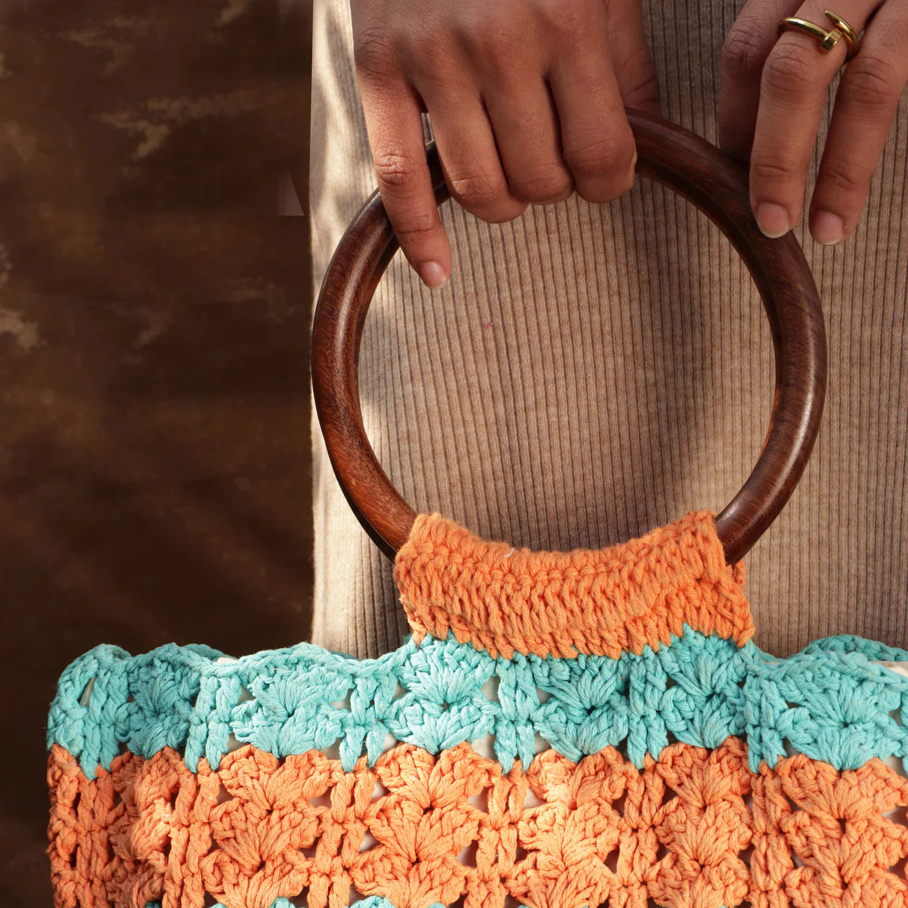 Step into colorful elegance with our rectangular hand-crocheted handbag, adorned with circular wooden handles, showcasing bright hues of orange, blue, and yellow for a playful touch.