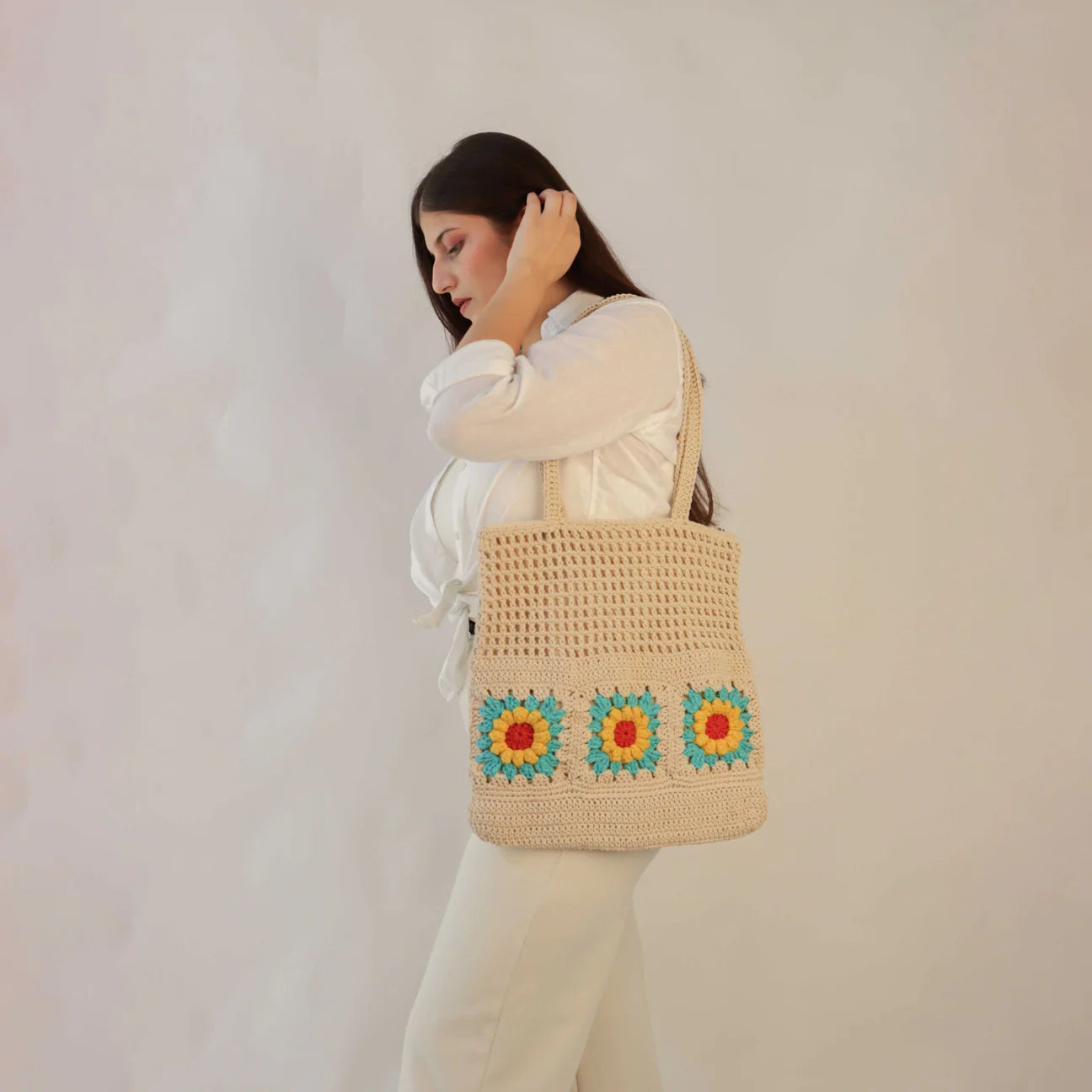 hand-crocheted tote bag featuring a spacious interior for your daily needs and adorned with delightful floral motifs in Off White, Red, Blue, and Yellow.