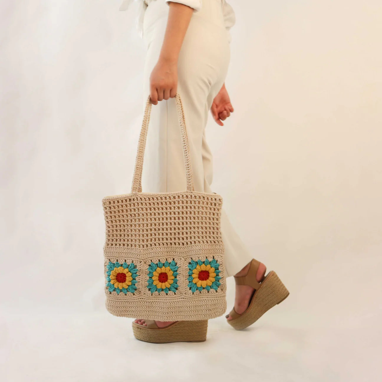 hand-crocheted tote bag designed to carry all your essentials, it comes adorned with charming floral motifs in Off White, Red, Blue, and Yellow.